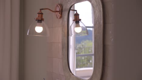 in a bathroom, view of the mirrors and the wall lamp in reflection, we see the reflection of the window seen on the luminous exterior in the mirror