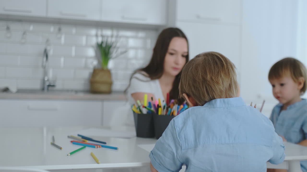 dos hijos de niños dibujan con su madre sentada en la cocina.