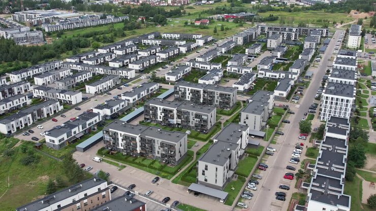 Luftaufnahme des Bezirks Pilaitė, die moderne Wohnblöcke im Vordergrund und ältere, graue Wohngebäude aus der Sowjetzeit im Hintergrund zeigt und die kontrastierende Architektur und Stadtentwicklung hervorhebt