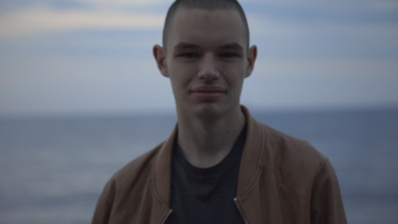 Portrait Of A Young Man Smiling Directly To The Camera With Blurry Blue Seascape Background - Closeup Shot