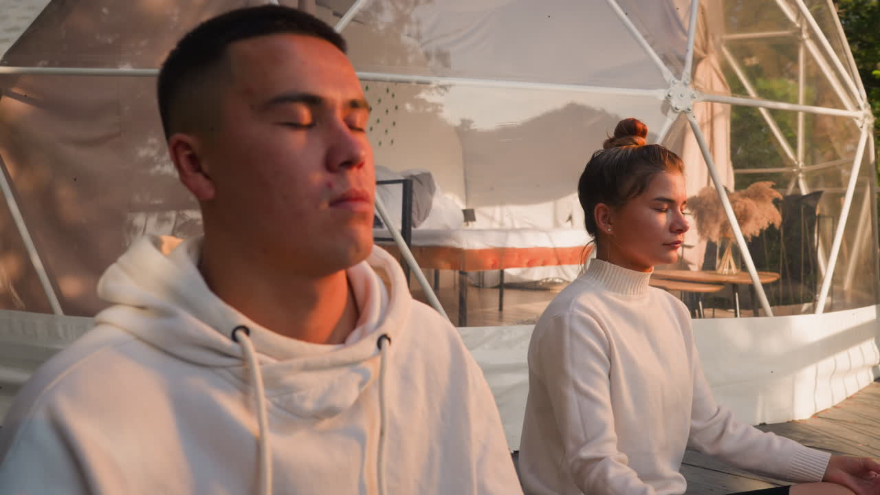 los jóvenes se sientan en la postura del loto en la tienda de glamping de cerca. la pareja enfocada termina el día con la práctica del yoga haciendo ejercicios de respiración. concepto de eco resort