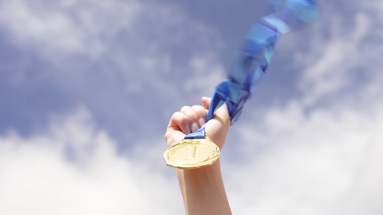 Raised hand holding a medal symbolizing success and achievement against the sky. Concept of winning, reward, recognition, and reaching goals in competition or life