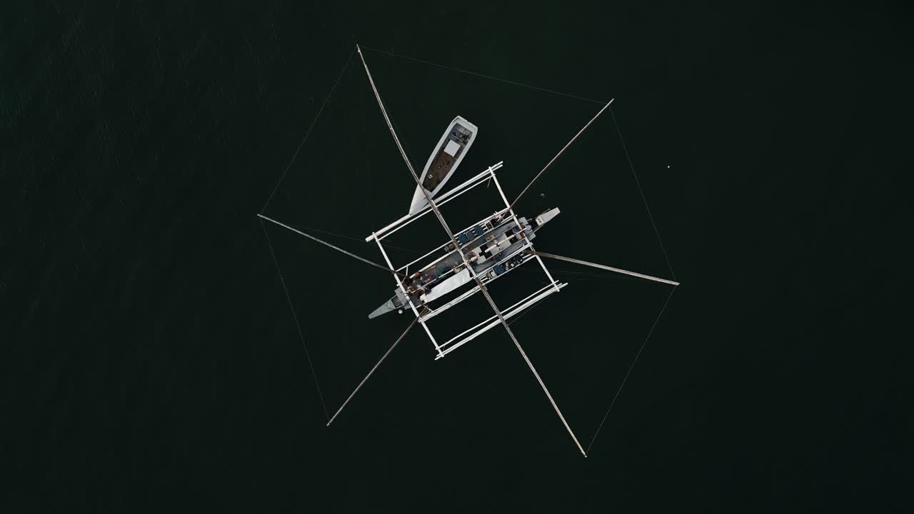 Top-down aerial orbit of double hull outrigger canoe with intricate network of fishing nets at Taloot Argao Port's pier and boats at sunrise in Cebu, Philippines, with calm waters