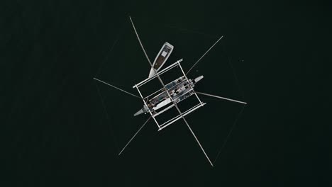 top-down aerial orbit of double hull outrigger canoe with intricate network of fishing nets at taloot argao port's pier and boats at sunrise in cebu, philippines, with calm waters