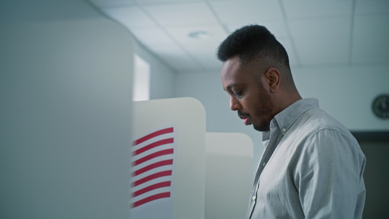 Nervous African American Male Voter Chooses which Presidential Candidate to Vote for Nervous African American Male Voter Chooses which Presidential Candidate to Vote for in Voting Booth at Polling Station us Citizen during National Elections Day in the United States of America