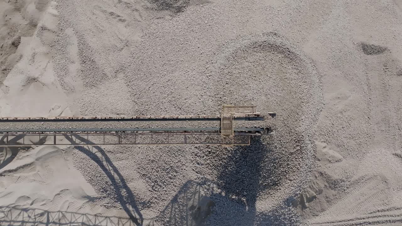 Top down aerial footage of rocks moving quickly on a conveyor belt before falling into a large pile.