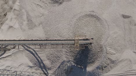 top down aerial footage of rocks moving quickly on a conveyor belt before falling into a large pile.