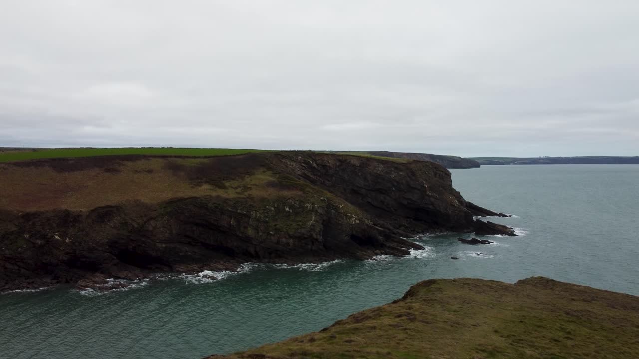 disparo de drone en la cima del acantilado empujando hacia el borde con olas marinas y espectacular costa rocosa de pembrokeshire reino unido 4k