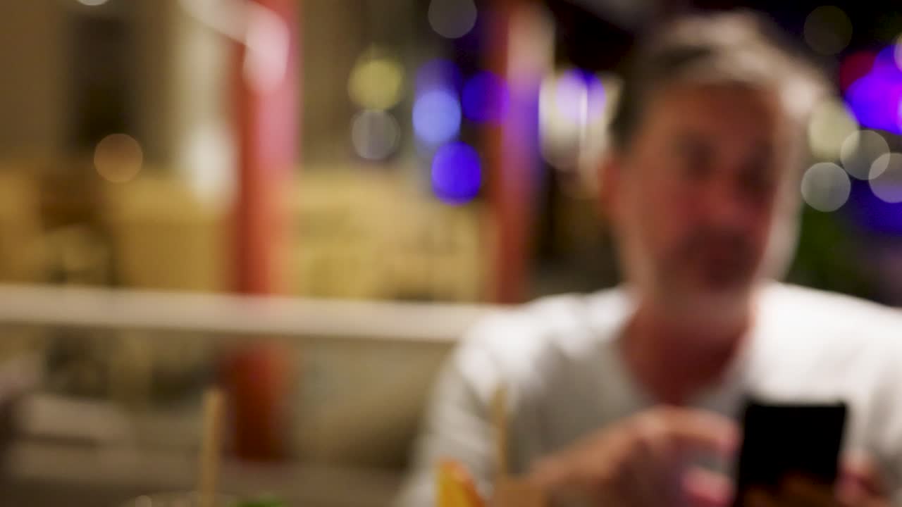 imagen borrosa de un hombre mostrando la pantalla del teléfono en un restaurante de phuket