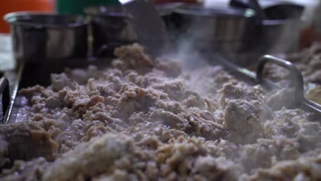 vendedor esparciendo tripas de carne con espátula a través de la plancha en preparación para tacos