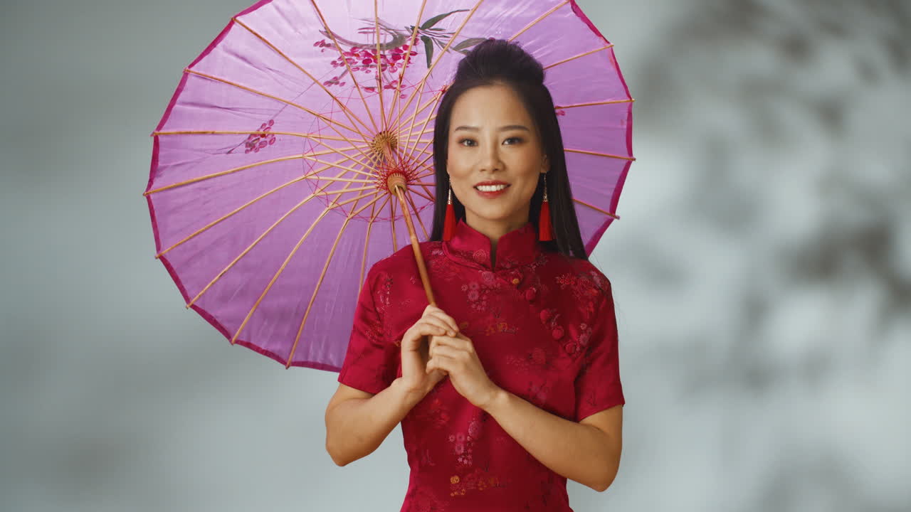 빨간색 전통 옷을 입고 파라솔을 들고 카메라를 보며 웃는 아시아 젊은 쾌활한 여성의 초상화