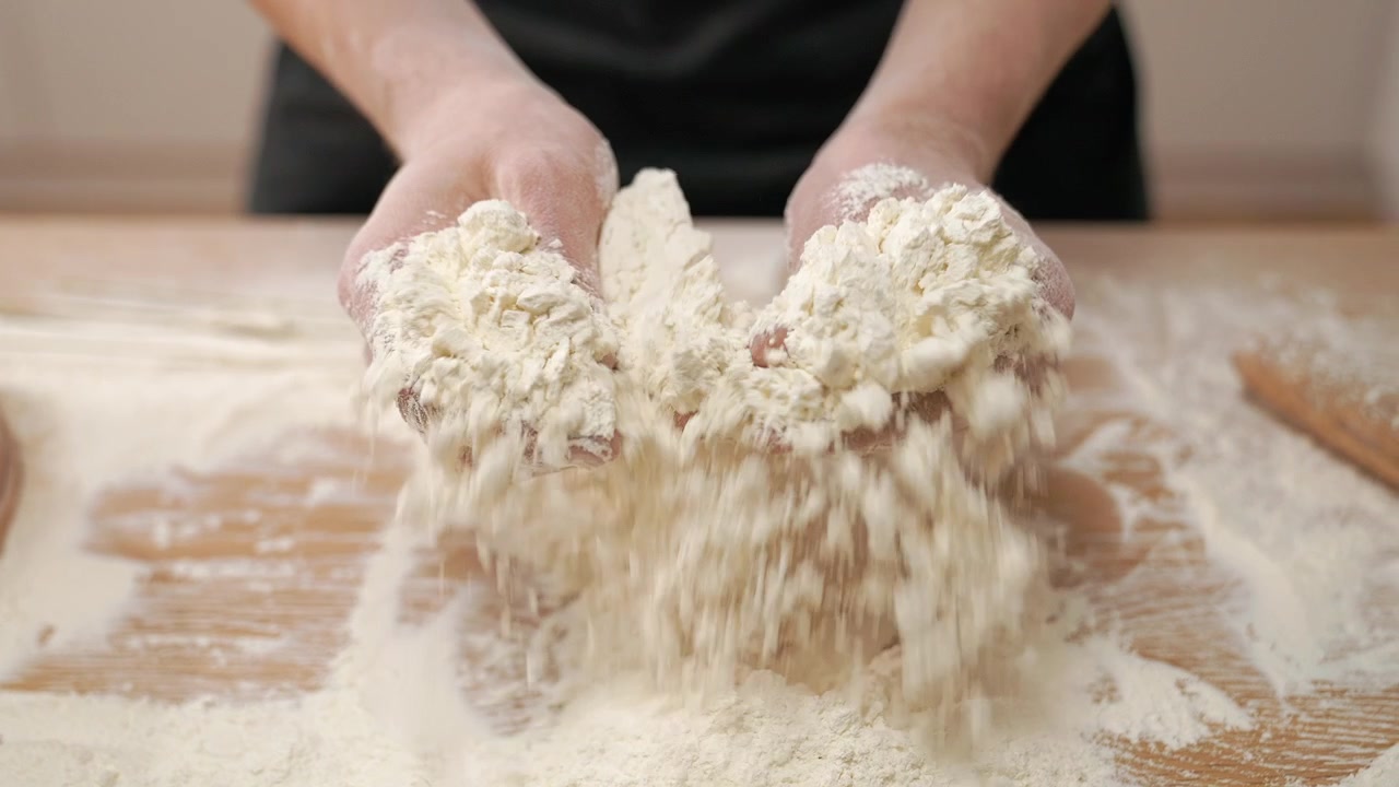 Primo piano di mani che setacciano la farina su un tavolo di legno