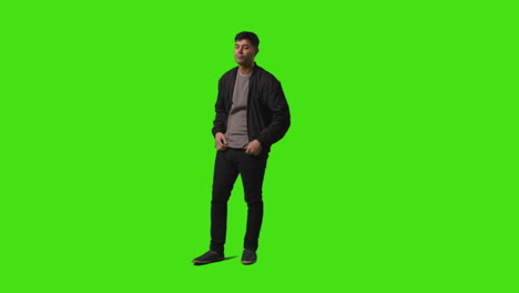 toma completa de un joven vestido casualmente sonriente de pie contra la pantalla verde cruzando los brazos y poniendo las manos en los bolsillos 2