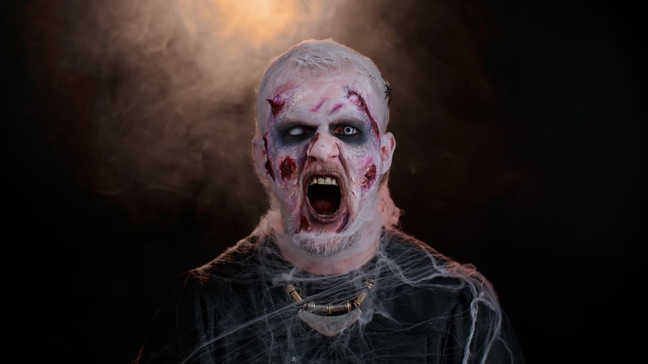 Sinister man in costume of Halloween crazy zombie with bloody wounded scars face screaming, shouting