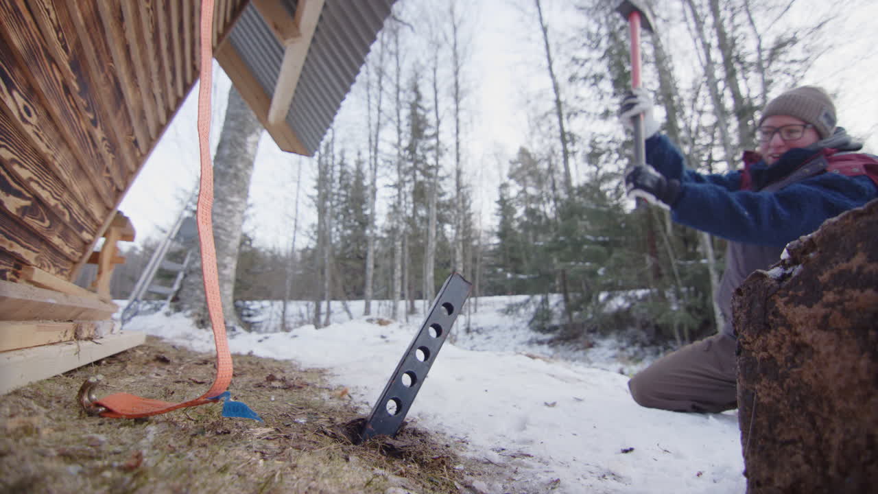 женщина забивает огромный стальной столб, чтобы привязать каюту до зимнего шторма.