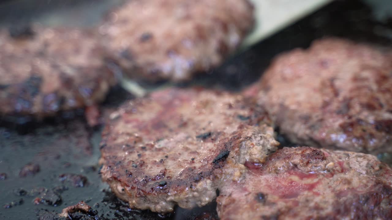 Hamburger beef meat sausage pork patties grilling on cast iron skillet grill cooked with propane at campsite outdoor barbecue with spatula moving around, close up shot