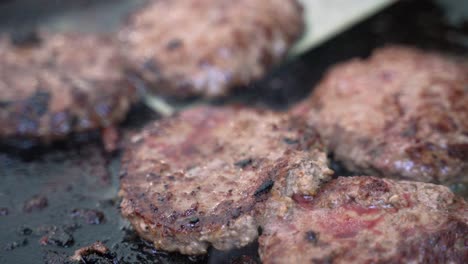 hamburger beef meat sausage pork patties grilling on cast iron skillet grill cooked with propane at campsite outdoor barbecue with spatula moving around, close up shot