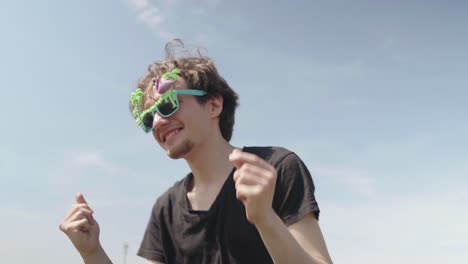 a young adult male dances to musical beat wearing crazy green glasses