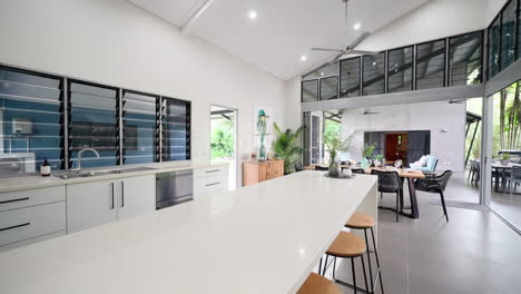 prestigous tropical style home kitchen dining area with open second floor balcony and round bar stools by open air entrance to patio