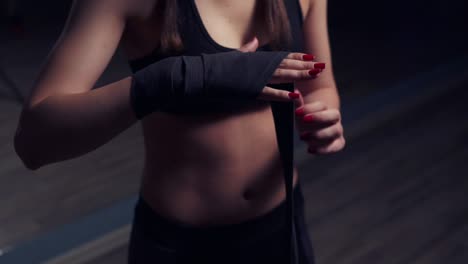 joven hermosa mujer envolviendo las manos con envolturas de boxeo negro en una habitación oscura. disparo en cámara lenta
