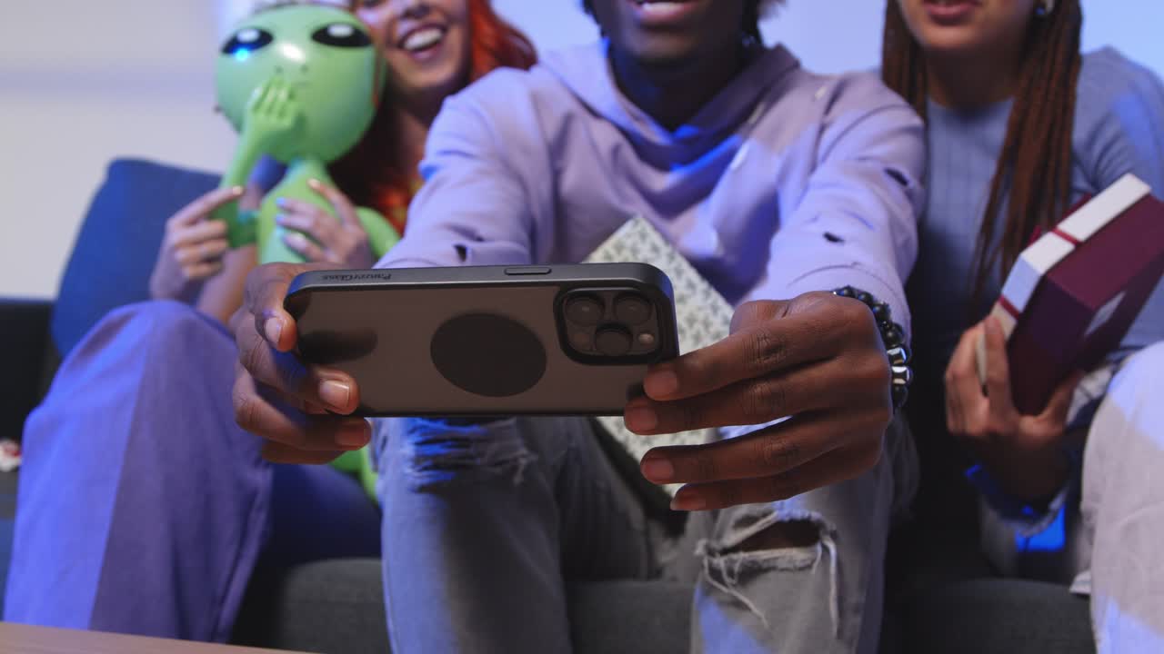 fotografía de estudio de amigos de la generación z en navidad sentados en el sofá con sombrero de papá noel y cuernos de renos tomando selfies en el teléfono móvil