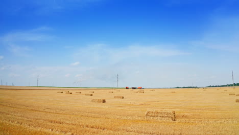 contrasting blue sky with yellow field of mowed wheat and hay bales on. fast approaching to the agricultural machinery standing in the field.