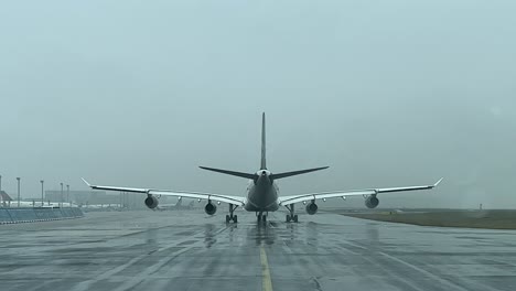 Vista-Trasera-De-Un-Airbus-A340-Gravando-Lentamente-En-Una-Calle-De-Rodaje-Durante-Una-Lluvia-De-Nieve
