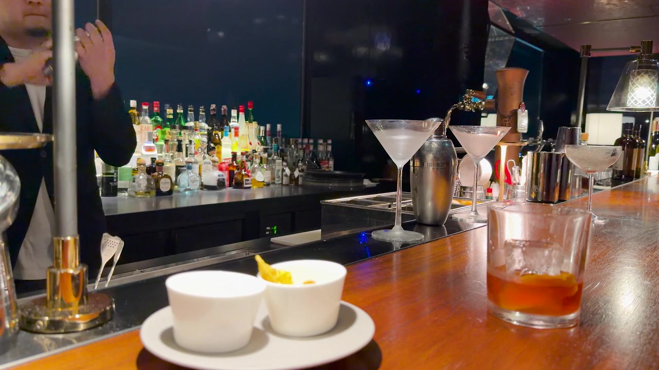 Một người pha chế đang lắc cocktail phía sau quầy gỗ với đồ uống và đồ ăn nhẹ ở Kanazawa.
