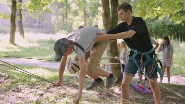 Children on a summer camp hike are moving along the ropes with the help of a guide who teaches children rock climbing and tourism. A boy in the forest overcomes a rope barrier