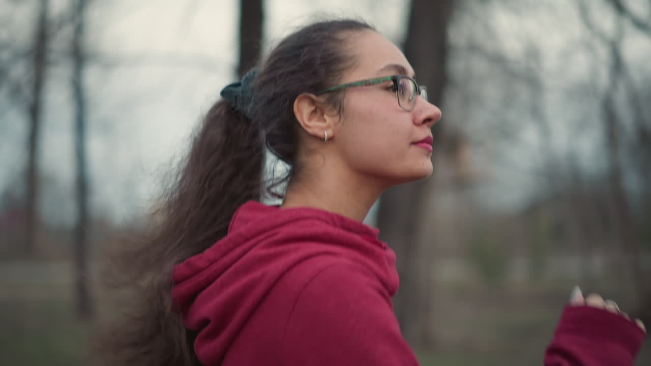 Female Runner Training, Active Woman In Red Hoodie Jogging With Focus And Calmness, Young Female Athlete Maintaining Steady Pace During Outdoor Endurance Exercise In Peaceful Park Setting