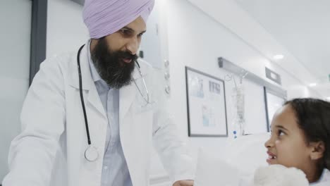 happy biracial doctor talking to sick girl patient in hospital bed in slow motion