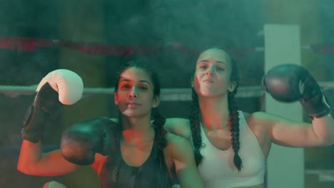 dos boxeadoras confiadas en coletas trenzadas sentadas cerca del ring, mirando a la cámara y mostrando bíceps