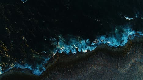 aerial top down perspective as whitewash ocean waves crash on rocky volcanic shoreline, curacao drone