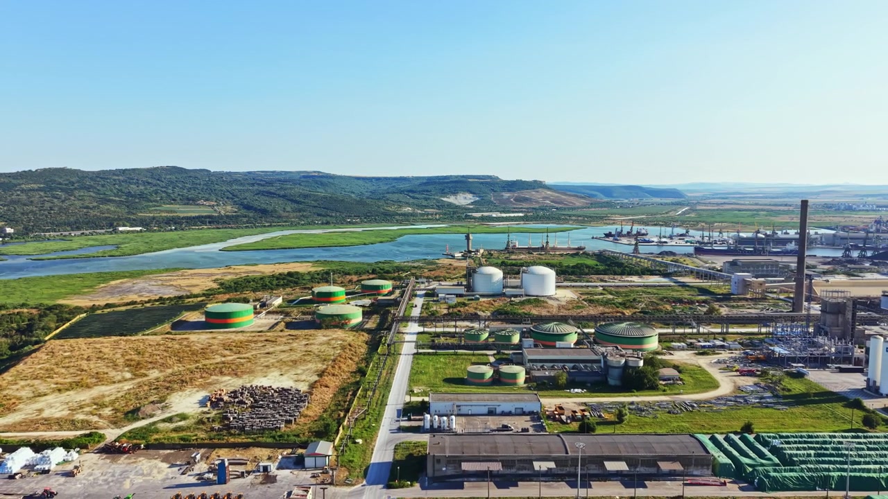 Aerial view of an industrial area near a river with storage tanks and machinery visible during a sunny day