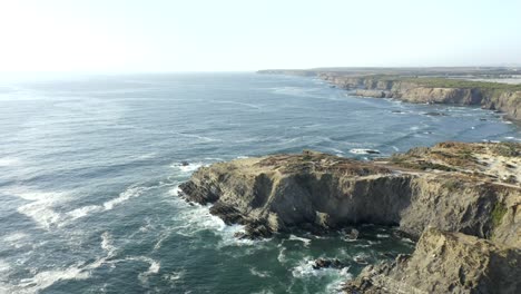 Ruhige-Drohnenaufnahmen-Vom-Flug-über-Die-Klippen-Von-Zambujeira,-Portugal,-Während-Die-Wellen-Gegen-Die-Küste-Schlagen