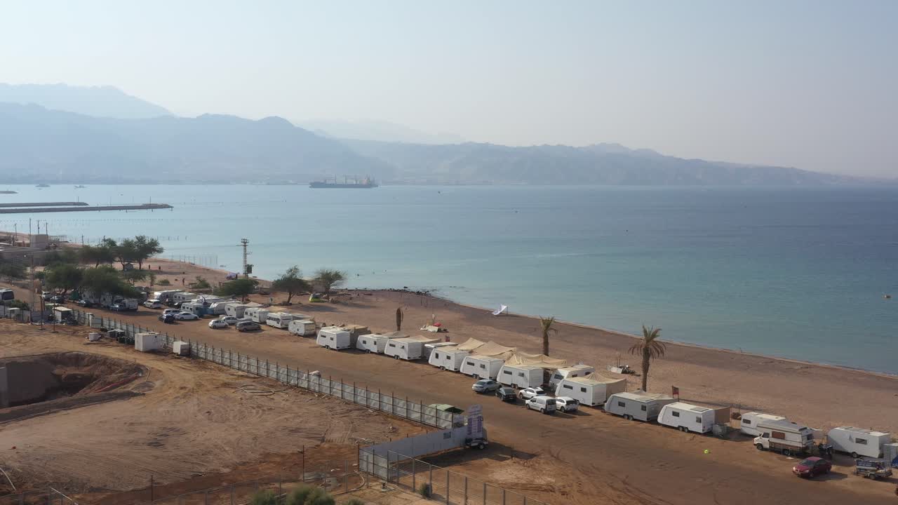 camping en la playa de hadatiyim con muchos autos de caravana estacionados en la costa en un día soleado, ciudad de eilat, israel - carretilla aérea a la derecha, que revela una plataforma autoelevadora para el envío en aguas poco profundas