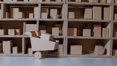 Miniature cardboard warehouse shelves filled with various sized boxes and a cardboard shopping cart loaded with merchandise represent the concept of online shopping and delivery logistics