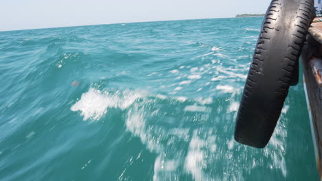 tire tied to hull of boat cruising on azure sea waves, action shot