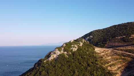 aerial reveal of ocean and greek island behind mountain during golden hour.