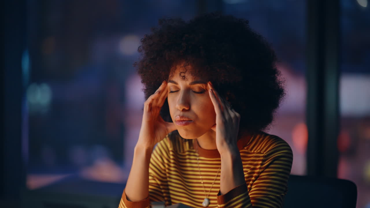 Tensed entrepreneur touching temples at dark corporate workplace closeup