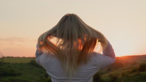 a young woman straightens her hair, stands in a picturesque place at sunset