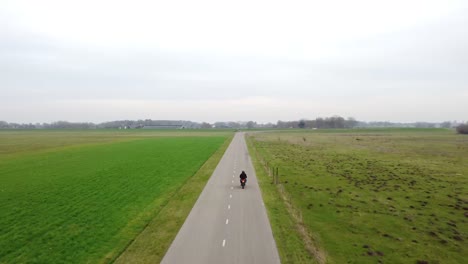 drone shot following motorcyclist on a small road between grass fields