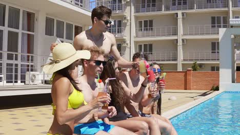 fröhliche gruppe junger freunde, die im sommer mit cocktails abhängen und sich am rand des pools unterhalten