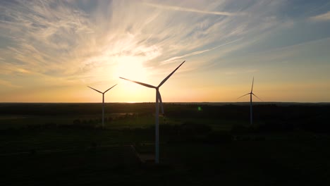 Grandes-Turbinas-Eólicas-Con-Palas-En-El-Campo-Vista-Aérea-Puesta-De-Sol-Naranja-Brillante-Cielo-Azul-Parque-Eólico-Giro-De-Drones-En-Cámara-Lenta