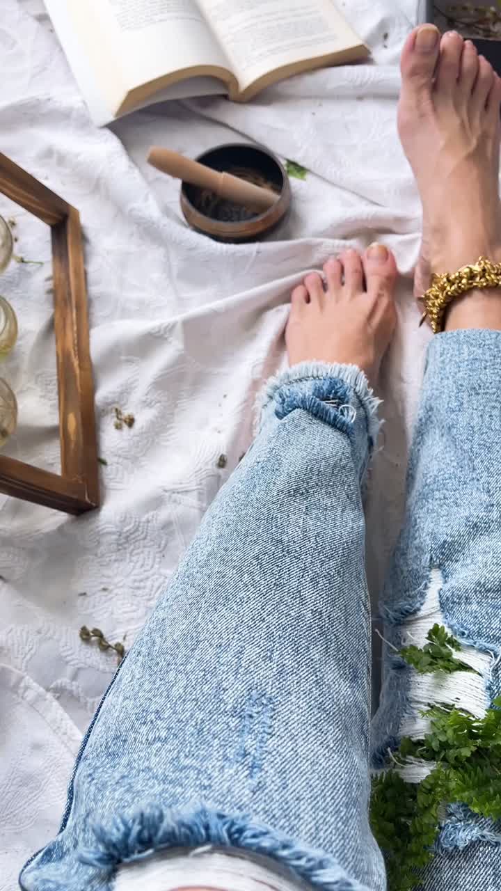 금색 발목걸이와 식물로 청바지를 입은 맨발의 여자