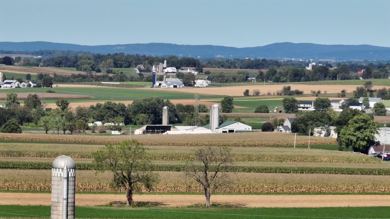 Aerial wide shot of agricultural fields and farmstead with silo storages. Blue sky in autumn season. Dolly shot. American suburb housing area. Peaceful landscape on sunny day