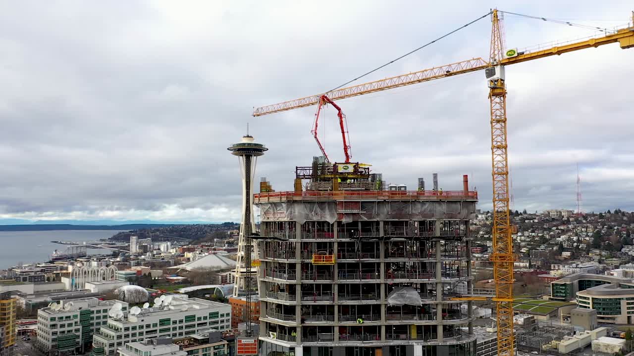 antena de un sitio de construcción de grúas creando un rascacielos con la aguja espacial de seattle en el fondo