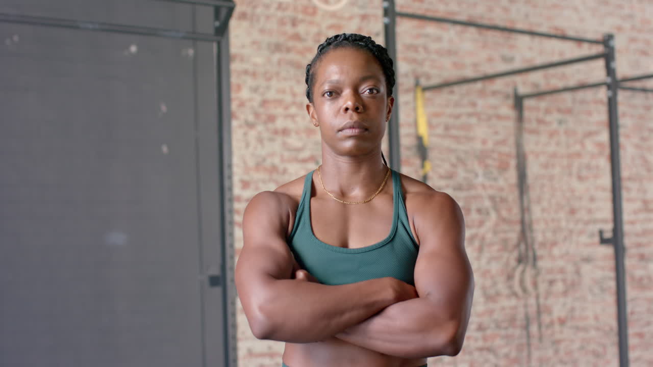 Confident female athlete crossing arms in gym, showcasing strength and determination