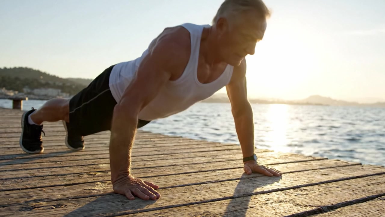 A Senior Man Engages in a Healthy Lifestyle by Performing Push-Ups at Sunset on a Wooden Pier, Embracing Fitness and Well-Being Amidst Natural Beauty