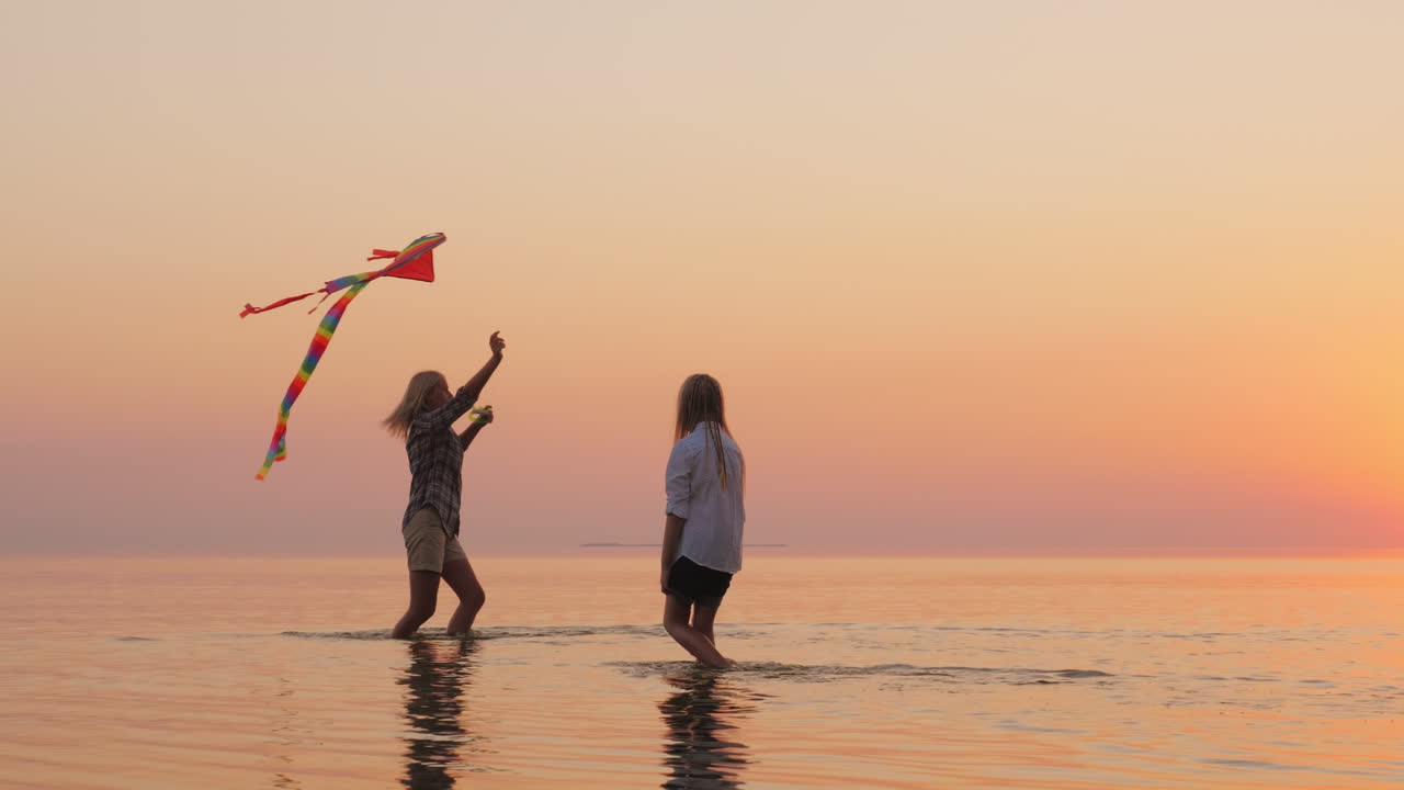 엄마와 딸이 아름다운 호수의 물 위에서 일몰에 연을 가지고 놀고 있습니다.